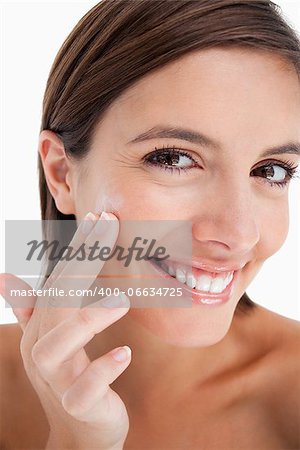 Attractive teenage girl applying moisturizer cream on her face with her fingers