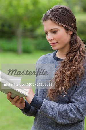 Young relaxed woman reading a book while standing upright in the countryside