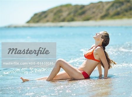 Happy young woman in swim suite laying on sea shore