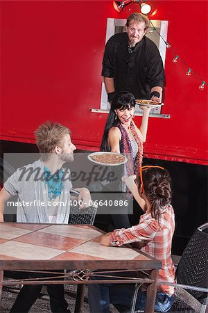 Friends receiving pizza orders from chef in canteen