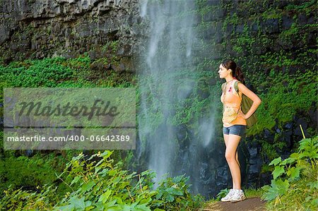 Young woman hiking in summer near waterfall.