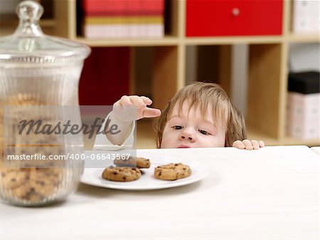 Photo of a nineteen-month-old stealing cookies from a plate on a table with a full cookie jar beside.