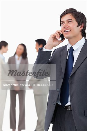 Salesman talking on mobile phone with team behind him against a white background