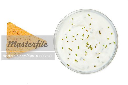 Bowl of dip with herbs beside a nacho against a white background