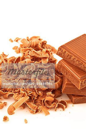 Many chocolate shavings beside a pile of chocolate against a white background