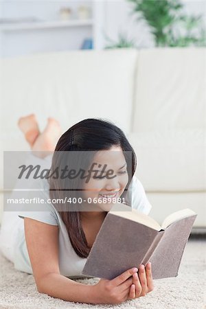 Woman lays on the floor as she reads a book in a living room