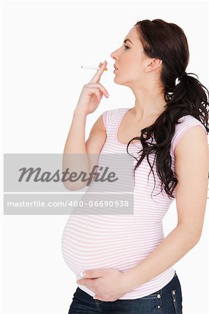 Young pregnant woman smoking against white background