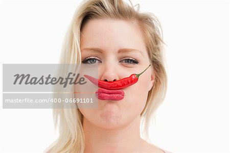 Blonde woman placing a chili between her nose and her mouth against a white background