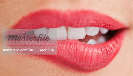 Close-up of the white teeth of a woman biting her lips