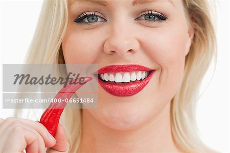 Happy blonde woman holding a chili against a white background