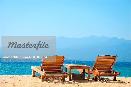 Beach chairs on perfect tropical yellow sand beach with blue sea and island on background, Gili, Bali, Indonesia
