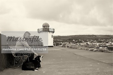 A mature man and his dog sitting by a light house