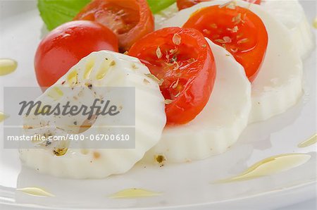 Fresh salad with goat cheese, tomato and basil pesto on a white plate.