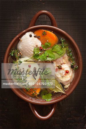 Chicken bouillon with vegetables and spices in a ceramic pot.