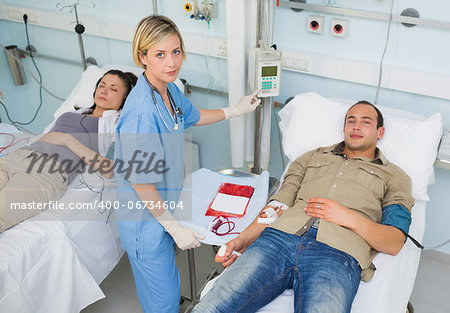 Nurse touching monitor next to transfused patients in hospital ward