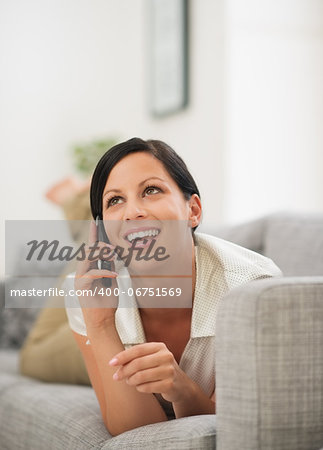 Happy young woman laying on couch and talking cell phone