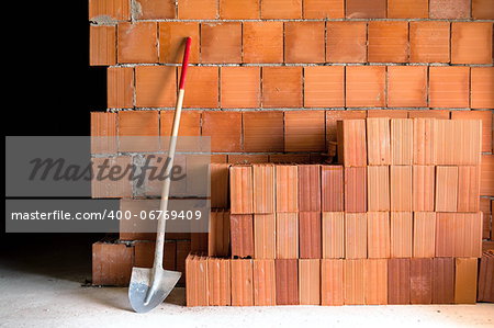 Brick wall with shovel, bucket and many bricks in a under construction masonry site