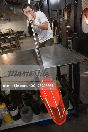 Latino artist blowing into tube with molten glass object