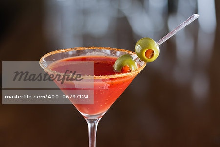 closeup of a bloody mary cocktail garnished with olives isolated on a busy bar top