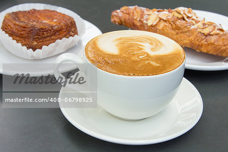 Cup of Caffe Latte with Almond Croissant and Flaky Pastry in Background