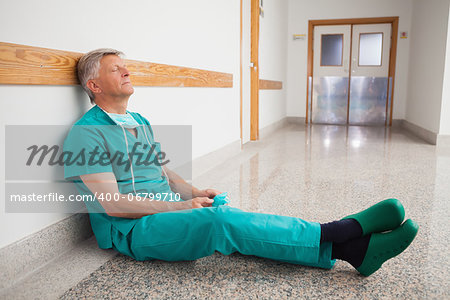 Doctor is sitting the floor of the corridor in the hospital while eyes closed