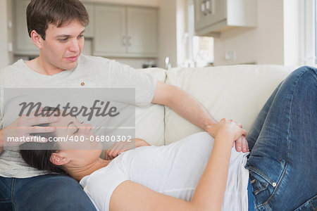 Pregnant woman resting on husband on sofa in living room