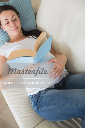 Young pregnant woman relaxing on the couch while reading a book