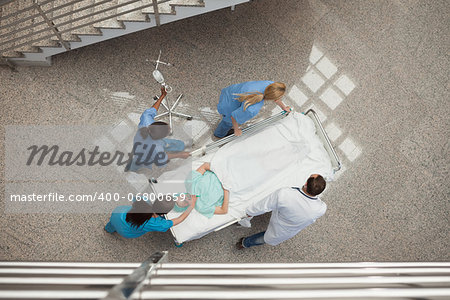 Three nurses and one doctor pushing one patient in a bed in hospital corridor