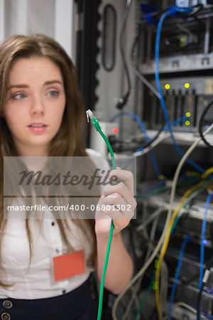 Woman holding green wire of server and looking confused in data center Woman holding green wire of server and looking confused in data center