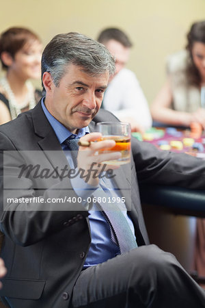 Man with cigar raising whiskey glass at roulette table in casino