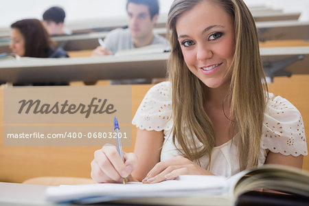 Woman sitting at the lecture hall while writing and smiling