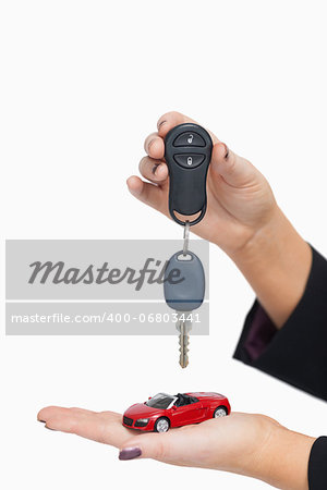 Woman holding key and small car against white background