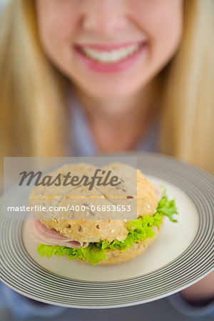 Closeup on plate with sandwich in hand of smiling teenager girl