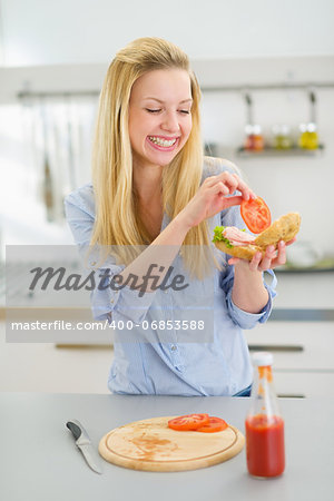 Happy young woman making sandwich in kitchen