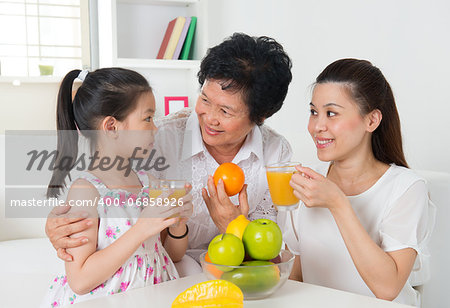 Asian family drinking orange juice. Happy Asian grandparent, parent and grandchild enjoying cup of fresh squeeze fruit juice at home.