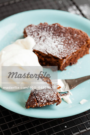 Closeup of slice of chocolate cake and whipped cream on plate resting on mesh metal tray