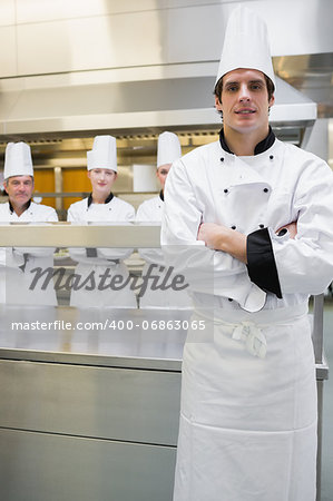 Chef standing with arms crossed with team behind him in the kitchen