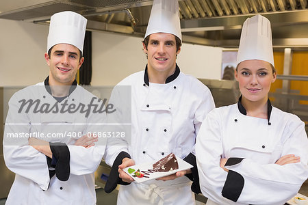 Three Chef's presenting a cake in the kitchen