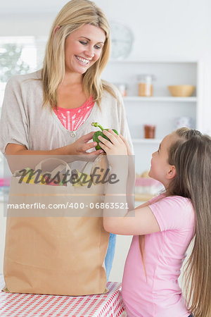 Woman giving green pepper to daughter from grocery bag in the kitchen