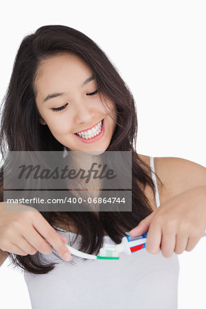 Woman smiling while holding a toothbrush and toothpaste against white background