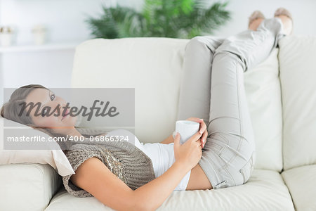 Calm woman lying on the sofa with a mug in the living room with her feet up