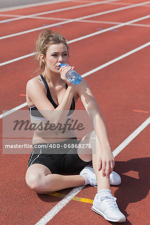 Blonde woman sitting on runing track and drinking bottled water