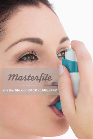 Brunette woman using astham inhaler against white background