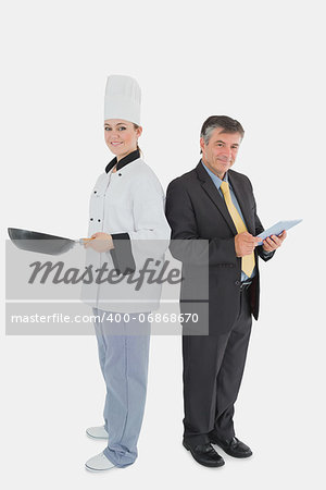 Full length portrait of happy businessman holding digital tablet and female chef with frying pan over white background