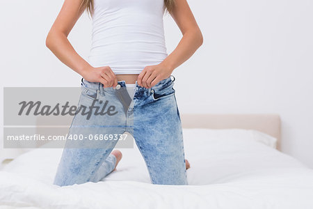 Woman trying to close her jeans on the bed