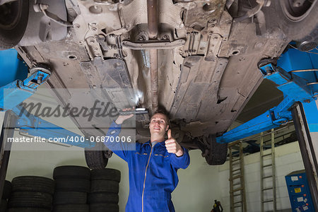 Portrait of young repairman under car gesturing thumbs up