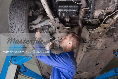 Repairman examining under car using flashlight