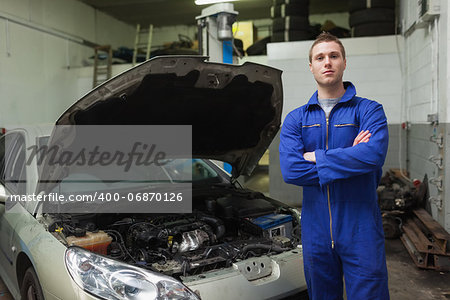 Portrait of confident auto mechanic standing by car with open hood