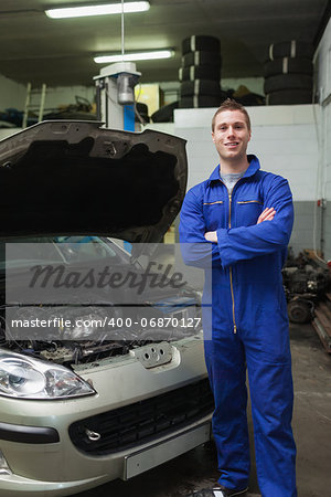 Portrait of young male mechanic with arms crossed standing by breakdown car