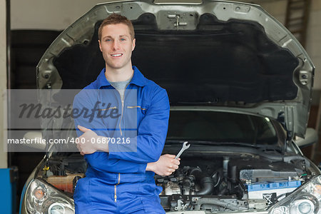 Portrait of confident mechanic leaning aganist car with open hood